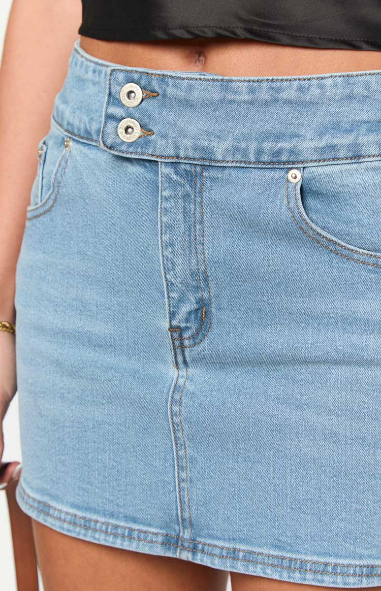 Close-up of the light wash denim mini skirt showing the double button waist closure and front pockets
