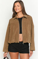 Close-up of a model wearing an open brown suede-like or corduroy jacket over a black ribbed top, with blue jeans and gold layered necklaces.