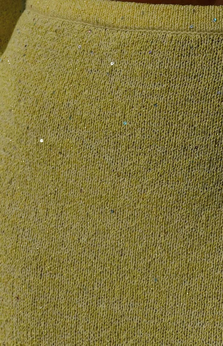 Close-up of the yellow knit maxi skirt fabric with a textured weave and scattered iridescent sequins