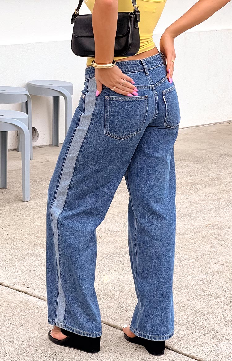 Back view of mid-wash denim low-rise wide-leg jeans- featuring a distinct lighter wash vertical stripe along the outer seams- offering a unique casual style.