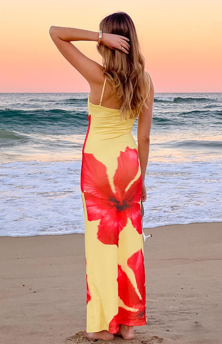 Rear view of the yellow maxi dress with thin spaghetti straps and a large red hibiscus print on the back skirt