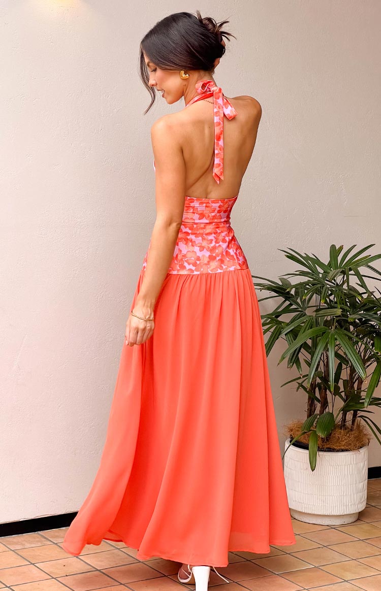 Rear view of a coral orange maxi dress featuring a pink floral halter neck, open back, and flowy skirt