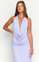 a woman poses in a purple cowl top and maxi skirt with a gold necklace and a corsage