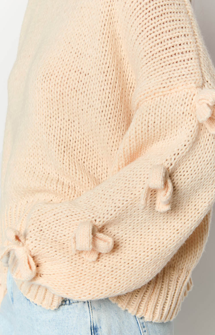 Close-up of the cream knit jumper sleeve with small bow details and ribbed cuff