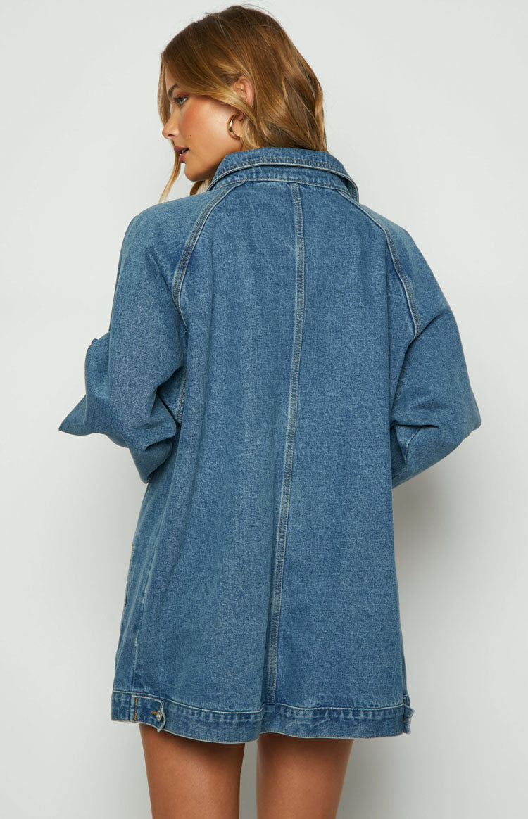 Rear view of an oversized blue denim jacket with raglan sleeves, visible stitching, and rolled-up long sleeves