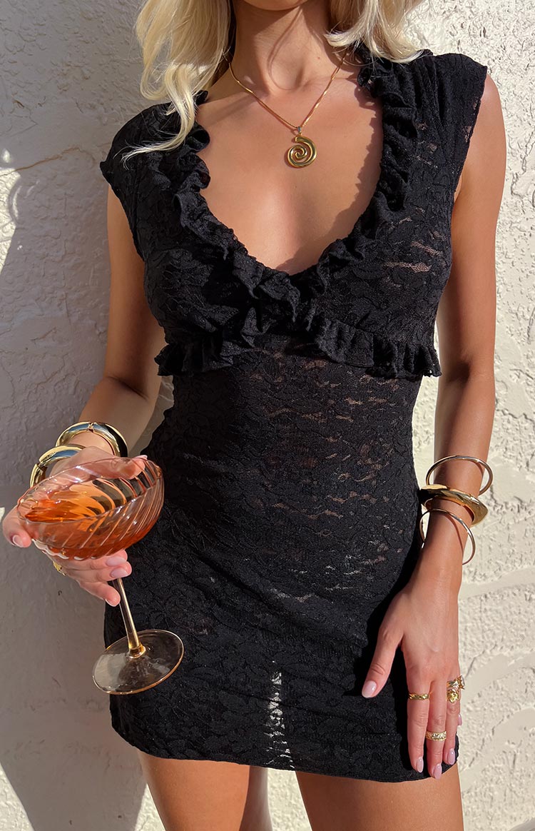 Close-up of the black lace mini dress showing the ruffled V-neckline, ruffled cap sleeves, and sheer lace fabric