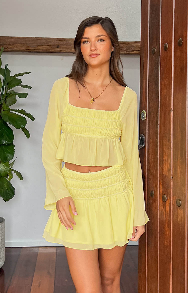 Front view of a yellow chiffon long sleeve top with a square neck, smocked bodice, and sheer flared cuffs