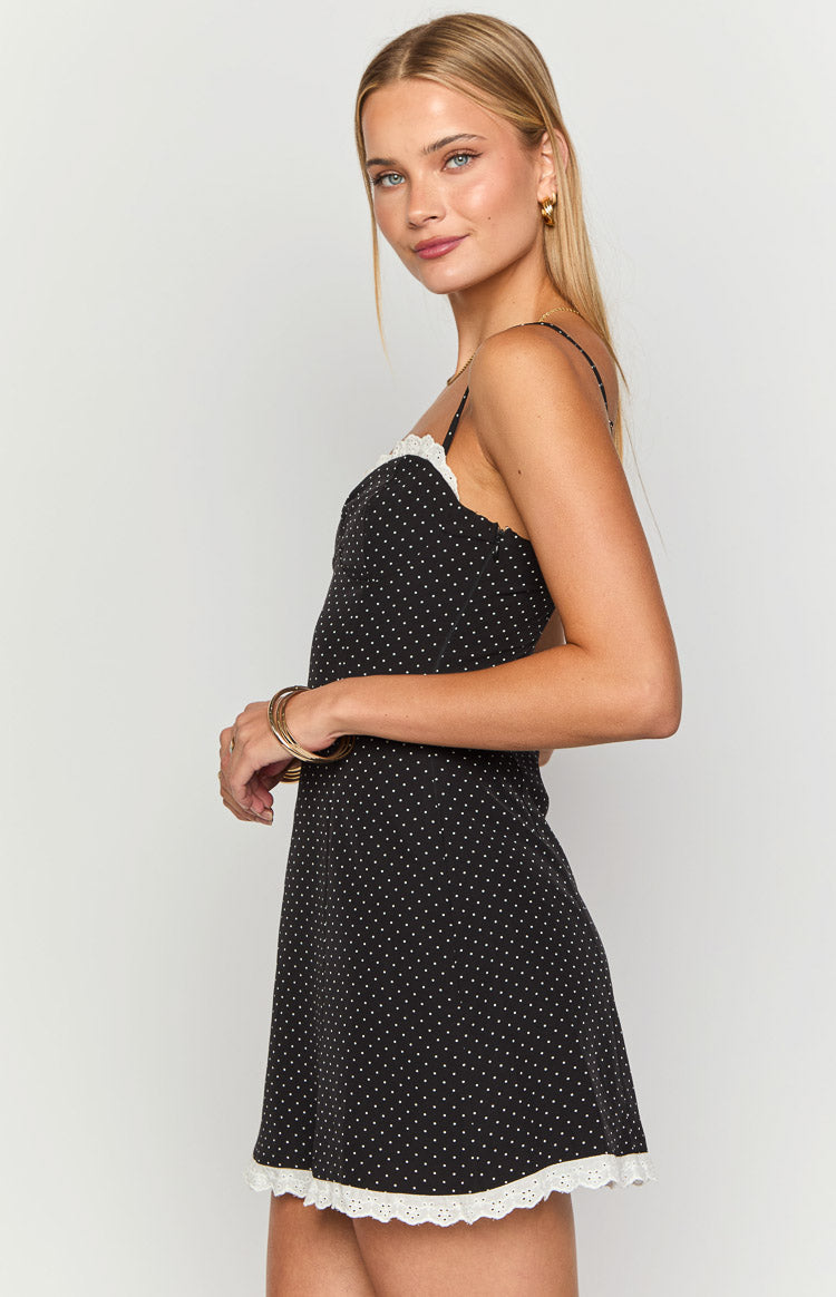 Side view of a black polka dot mini dress with white lace trim on the neckline and hem, featuring thin spaghetti straps
