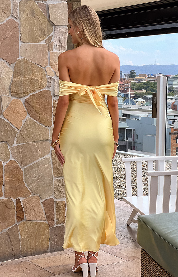 Back view of a yellow satin off-the-shoulder maxi dress featuring a large bow tie and ruched bodice