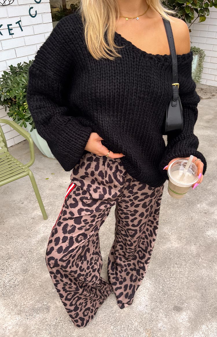 A loose-fitting black off-the-shoulder knit sweater paired with brown and black leopard print wide-leg pants featuring red and white racer stripes down the side.