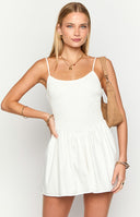Model wearing a white mini dress with a fit and flare silhouette and shirred material through the bodice- styles with a brown bag and brown boots