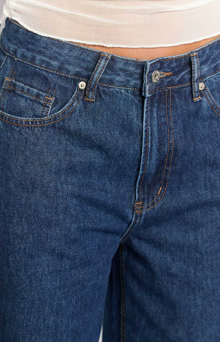 Close-up of the dark wash denim jeans showing the button fly, front pockets, and contrast stitching