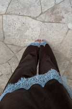 Close-up of the light blue scalloped lace trim on the hem of brown satin pants