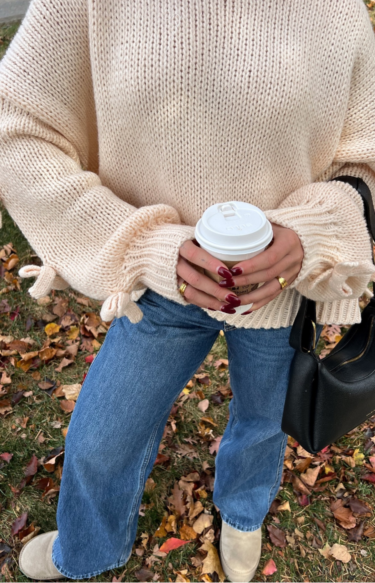 Close-up of the cream chunky knit jumper showing the tie-cuff detail on the long sleeves