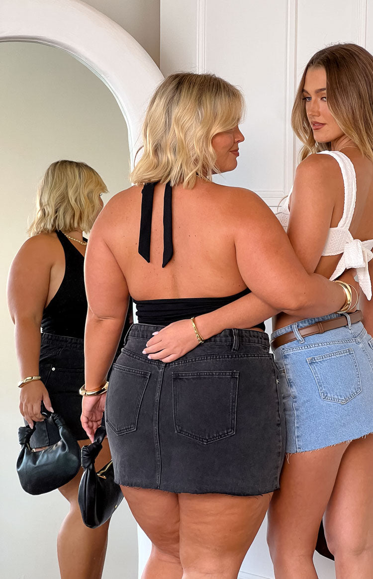 Rear view of a black denim mini skirt with two back patch pockets and a raw frayed hem