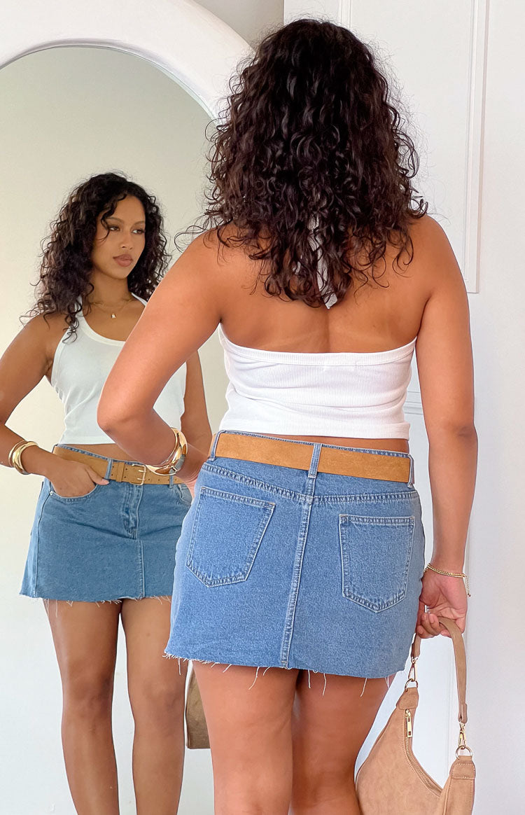 Rear view of a mid wash denim low rise mini skirt with back patch pockets and a frayed hem
