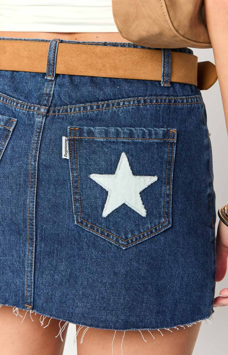 Close-up of the white star appliqué on the back pocket and frayed hem of a blue denim mini skirt