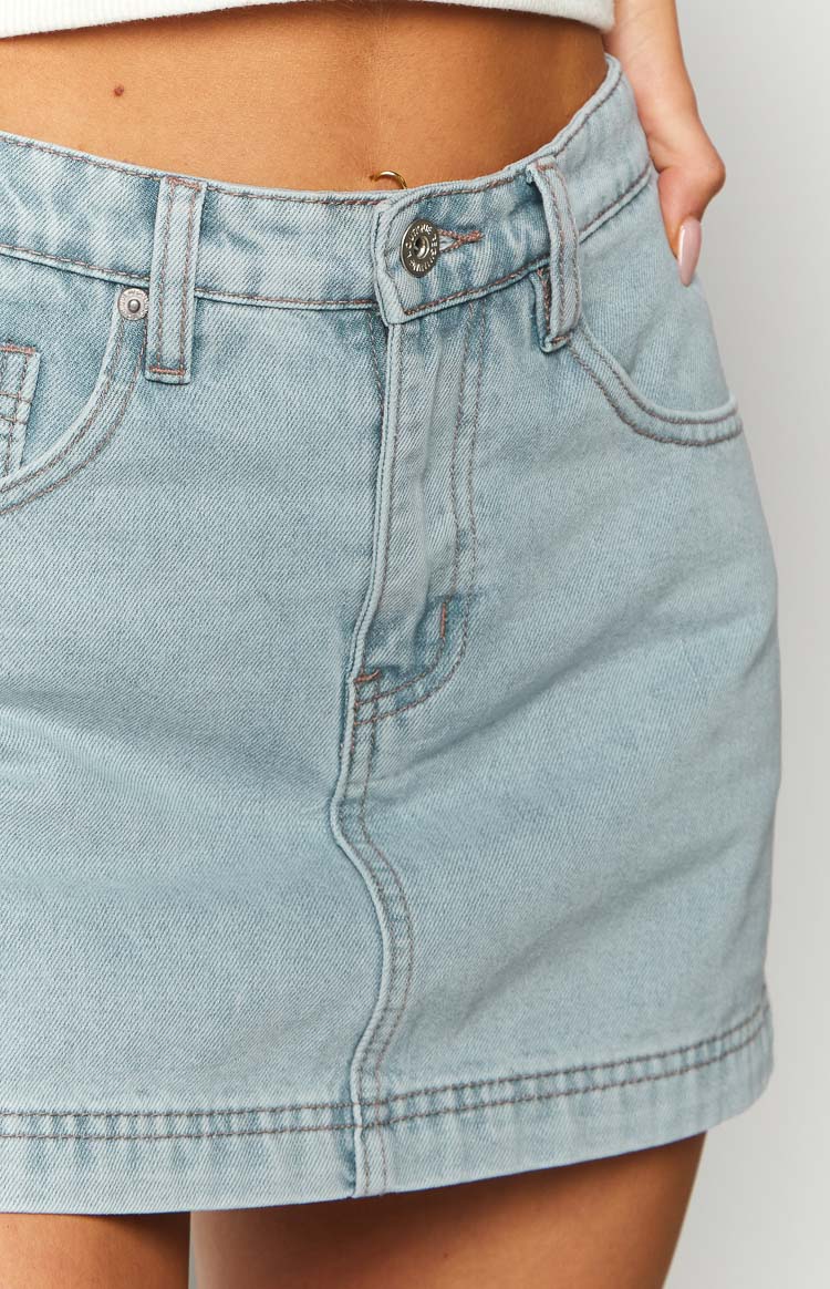 Detail shot of the light wash denim skort's waistband, silver button closure, belt loops, and front pockets