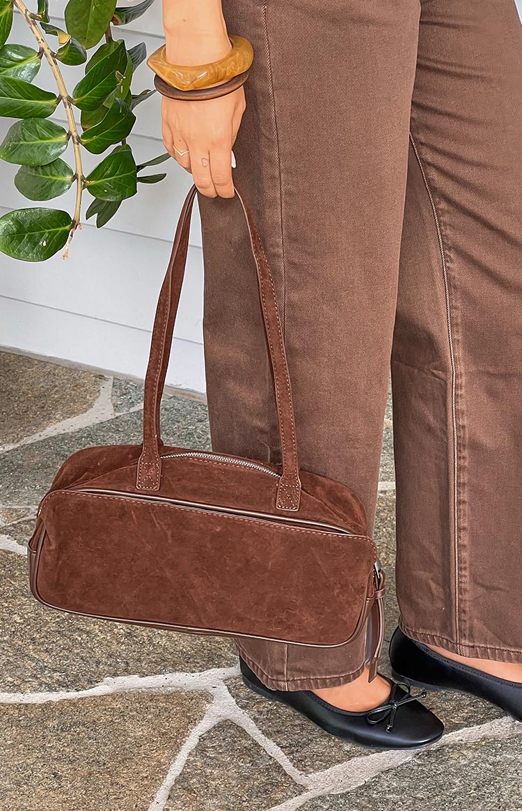 Close-up of a brown suede baguette bag showing the silver zipper and piping detail