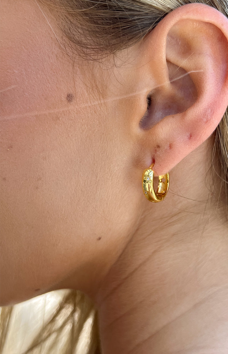 Close-up of a gold hoop earring featuring small star shapes with tiny clear gems