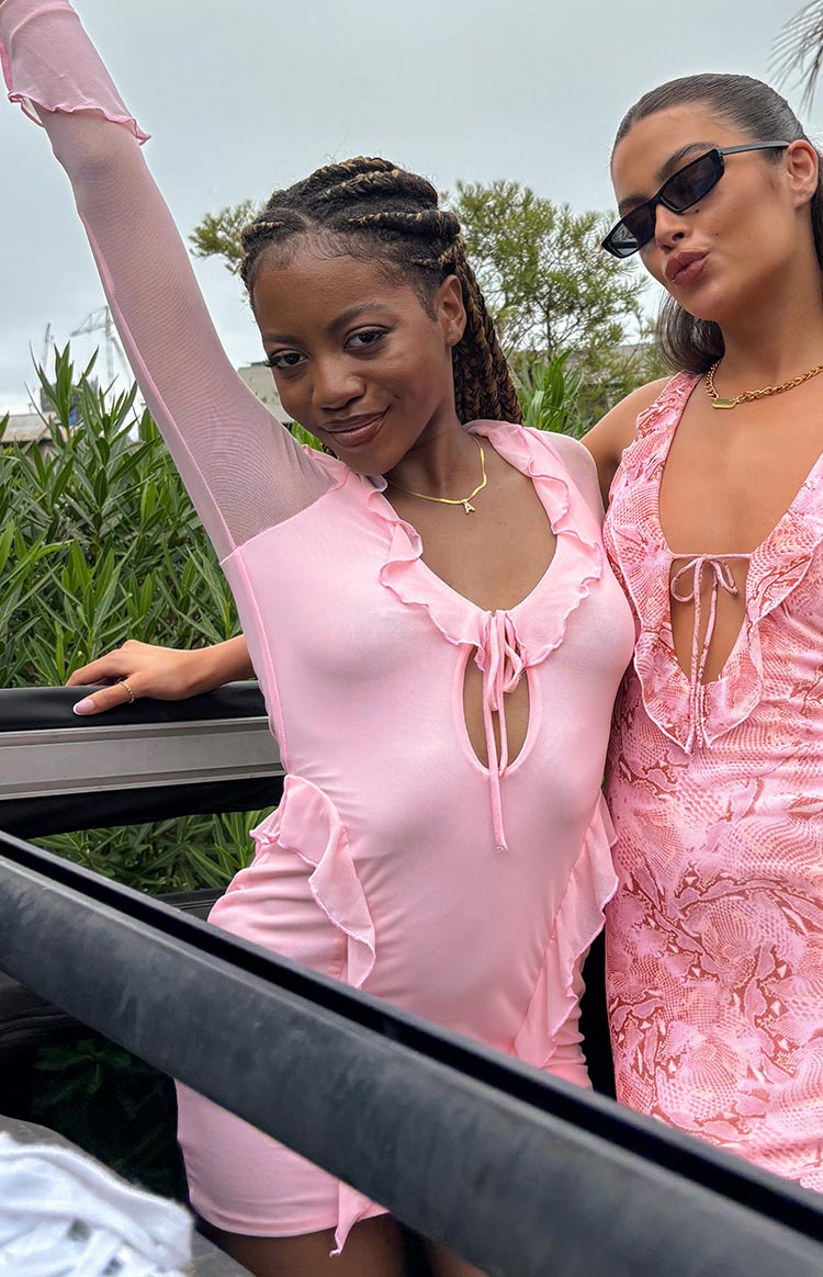 Close-up of pink mesh mini dress showing V-neck with tie-front cutout, ruffle trim, and sheer long sleeves