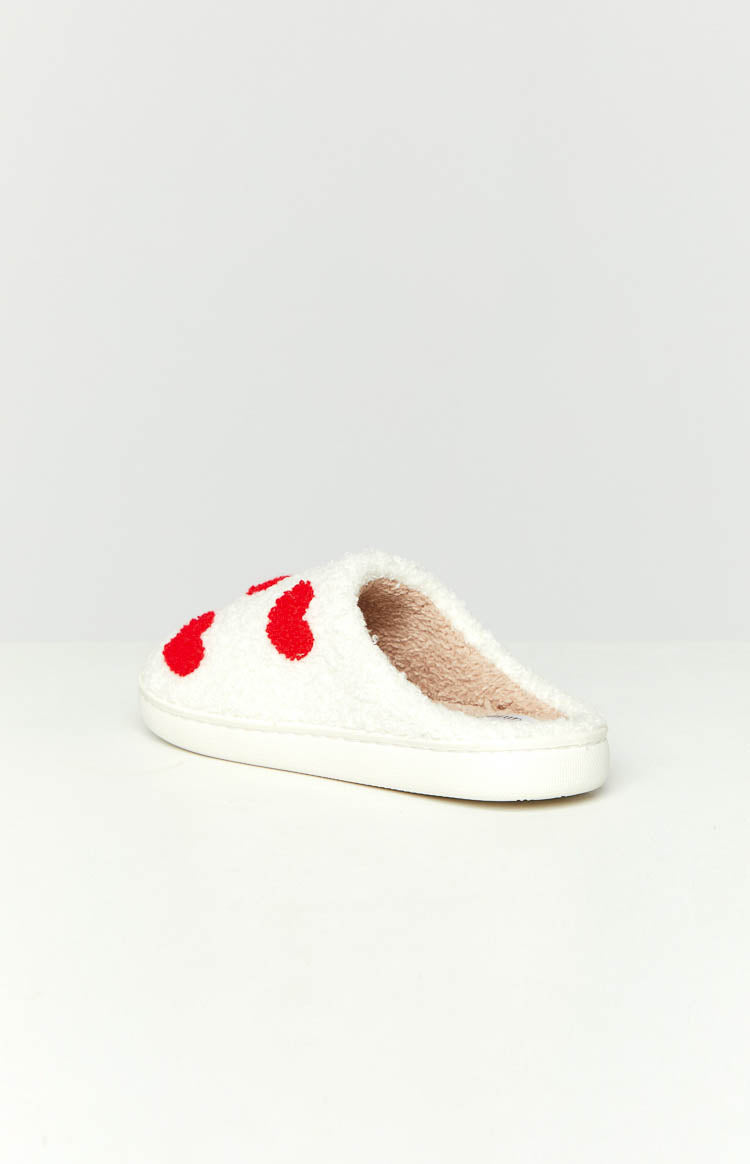 Side view of a white fluffy slipper with red heart pattern and a beige fluffy interior