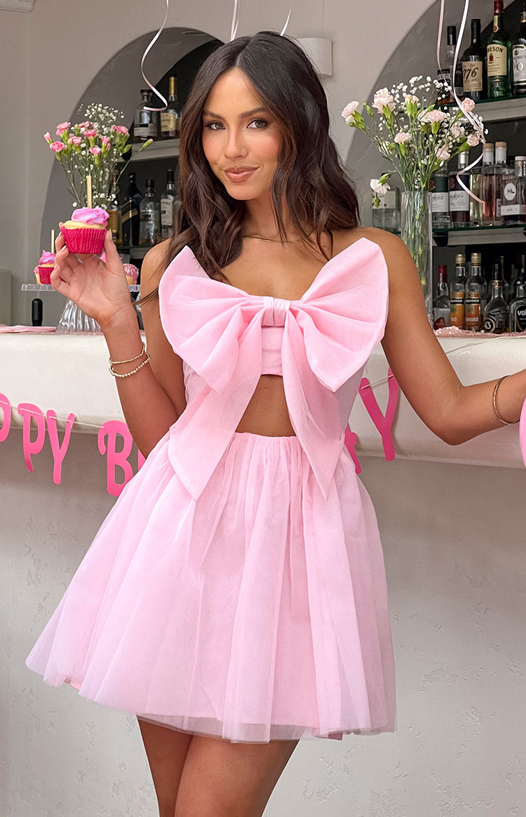 Pink strapless mini dress featuring a large tulle bow on the bust, a waist cutout, and a full layered skirt