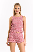A close-up of a vibrant red and white gingham two-piece set- featuring a shirred- sleeveless top with a ruffled hem and matching shirred shorts with ruffled edges- perfect for a playful summer day.