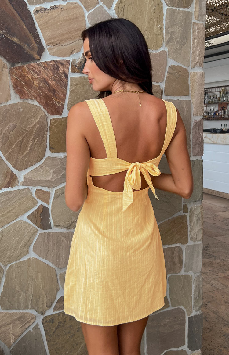 Rear view of a yellow mini dress showing the tie-back detail, side cutouts, and textured fabric