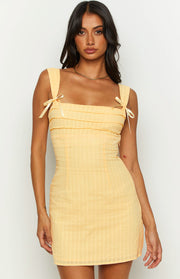 Close-up of the yellow mini dress showing the square neckline, bow-tied straps, and pintuck bodice with lace trim