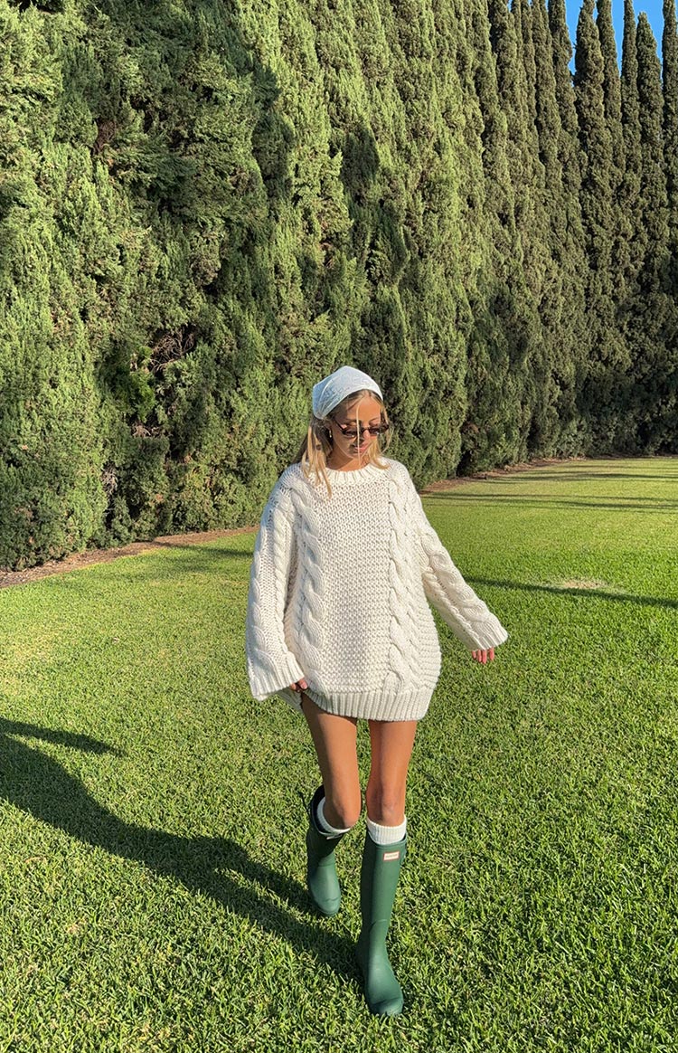 Cream cable knit sweater dress with oversized fit, round neck, wide sleeves, and ribbed hem