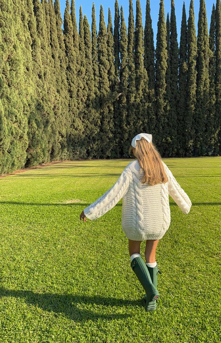 Rear view of a cream cable knit sweater dress with chunky vertical cable patterns on the back and long sleeves