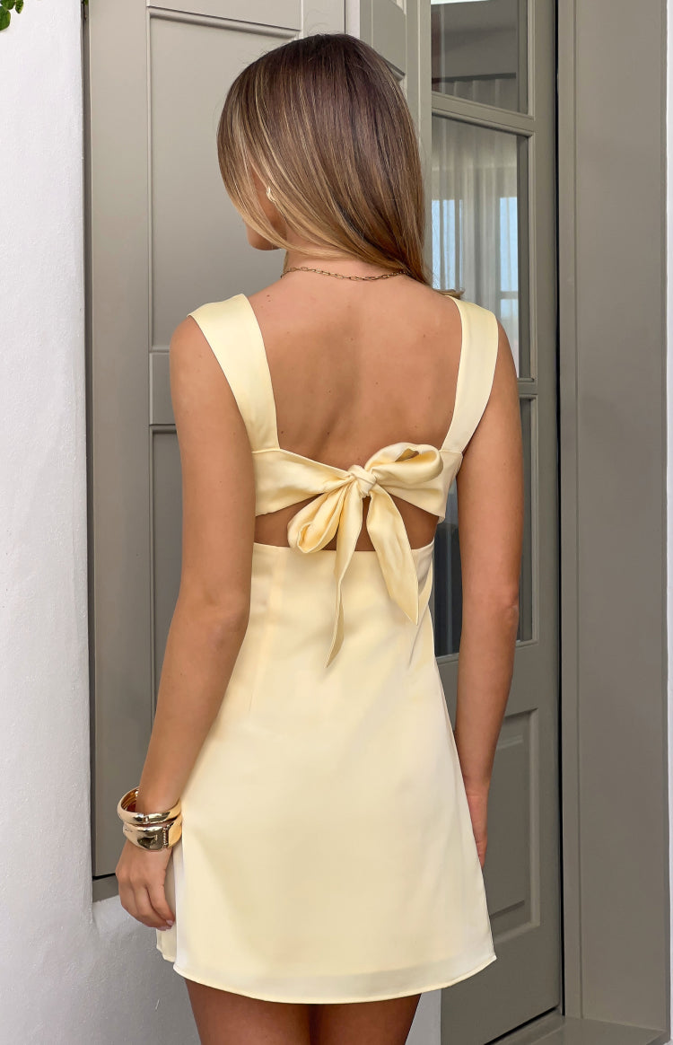 Rear view of a yellow satin mini dress with a large bow detail at the back and waist cutouts