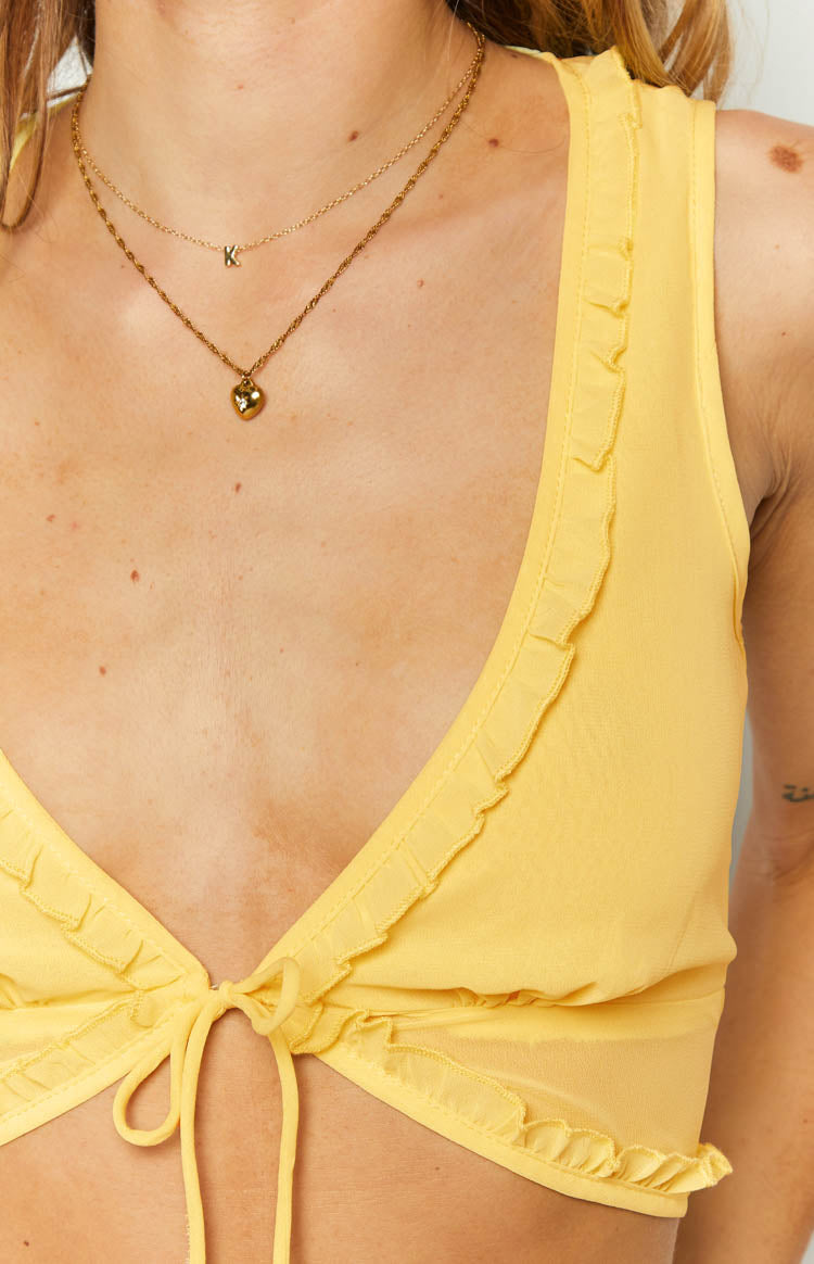 Front close-up of the yellow tie-up crop top with a central bow closure and ruffled trim on the V-neckline and bottom edge