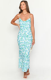White maxi dress with blue floral print, a draped cowl neckline, and a body-skimming fit