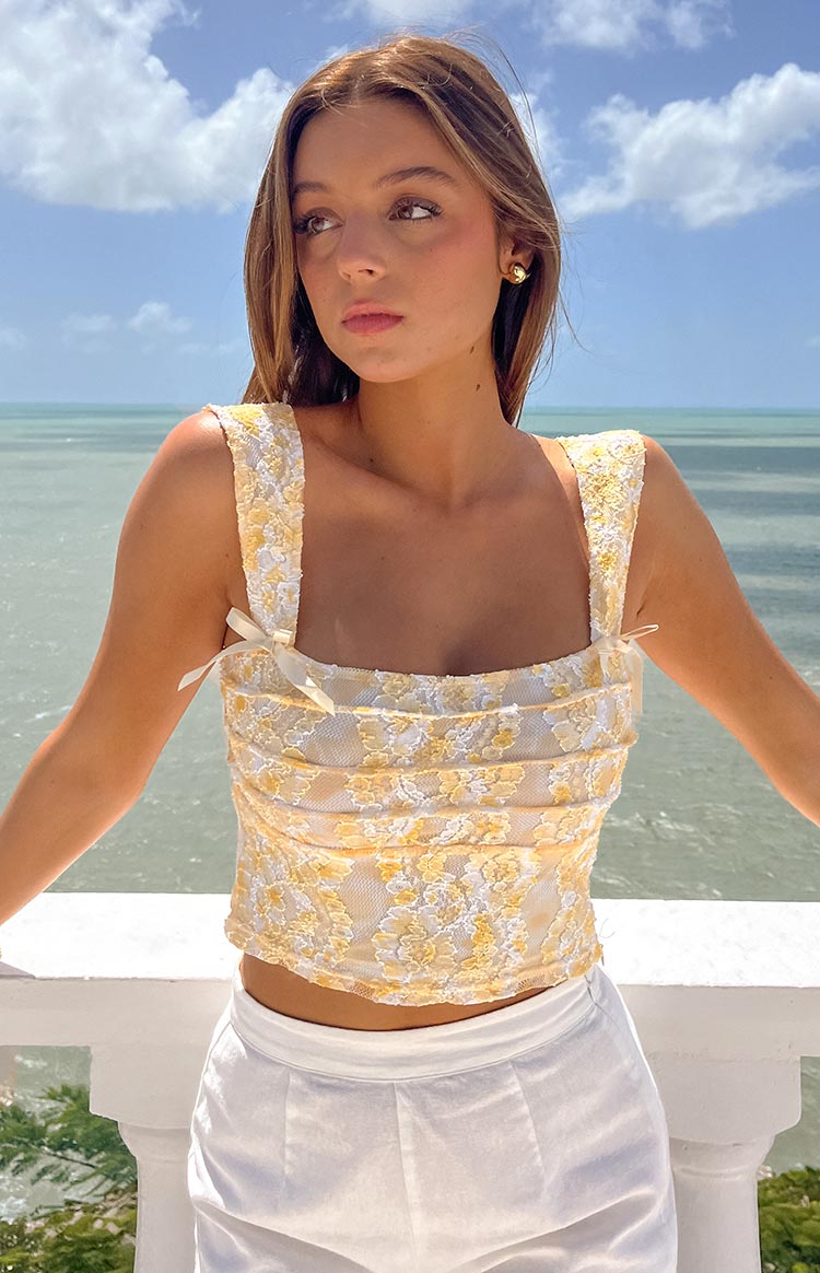 Front view of a yellow lace crop top with a square neckline, wide straps, and small white bows