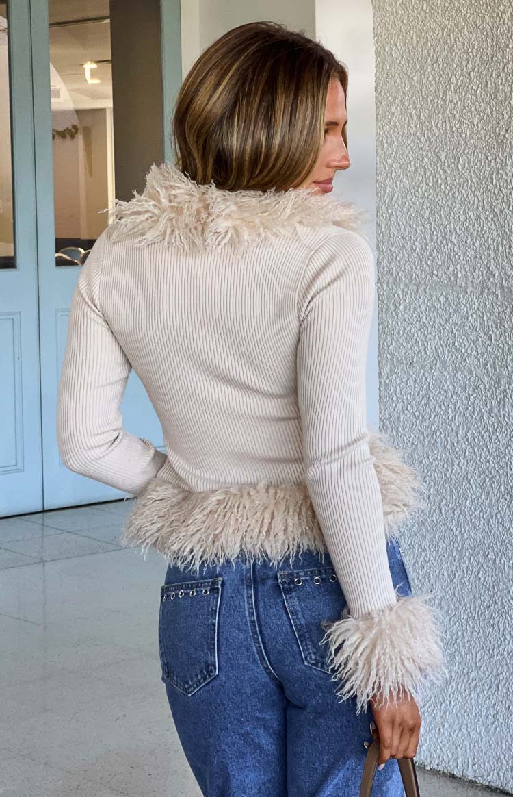 Rear view of a beige ribbed knit cardigan with shaggy fur trim on the collar, hem, and cuffs