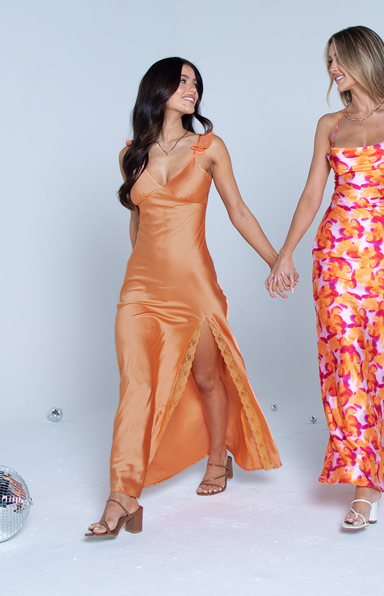 Orange satin maxi dress with a V-neck, bow shoulder straps, and a high leg slit revealing lace trim
