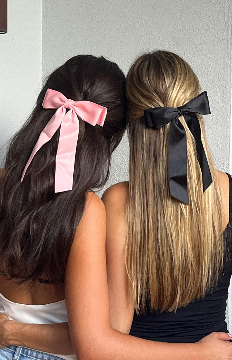 Rear view of a pink satin bow hair clip with long flowing tails, secured at the back of dark hair