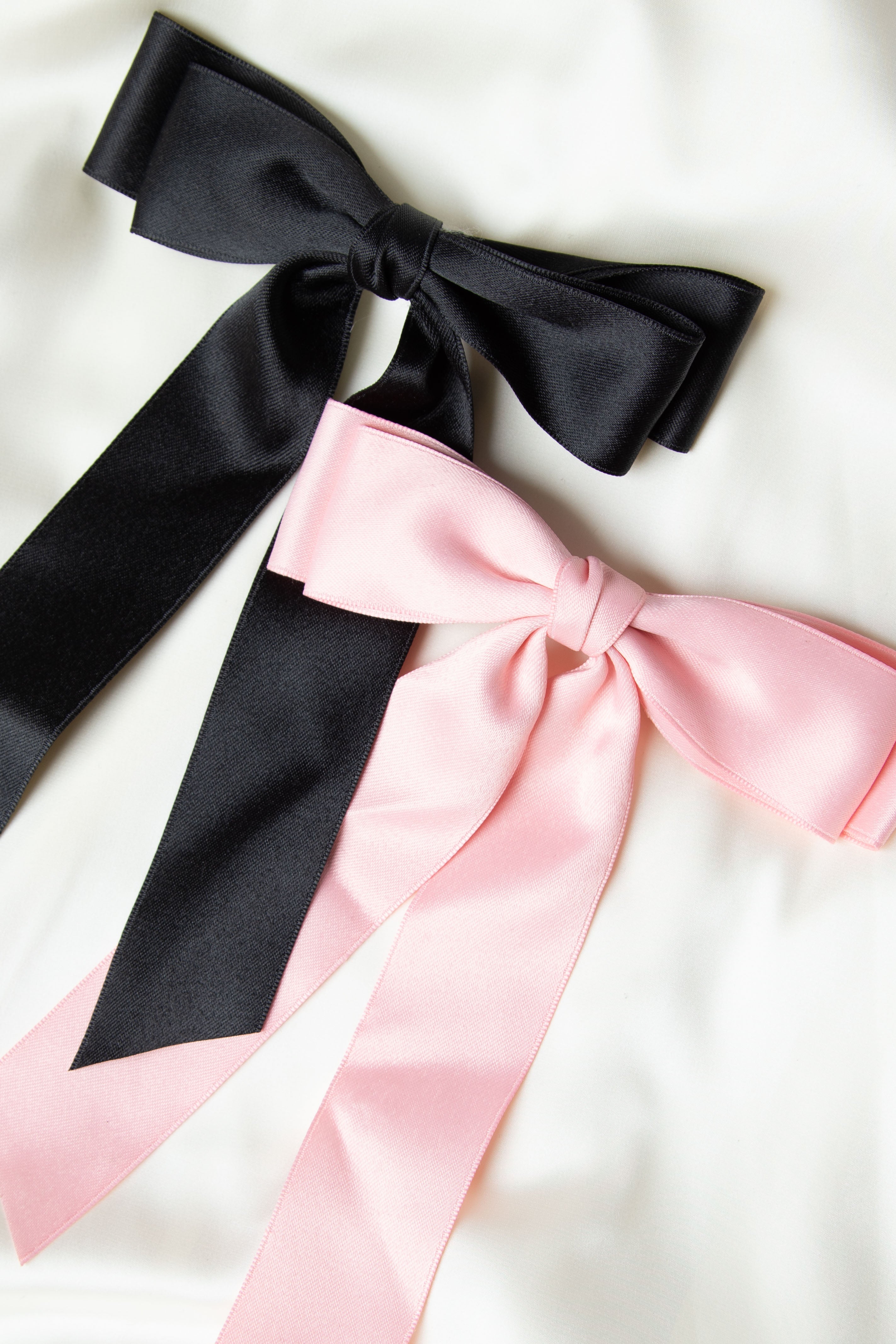 Light pink satin bow and black satin bow side by side, showcasing the smooth fabric and neatly tied knot