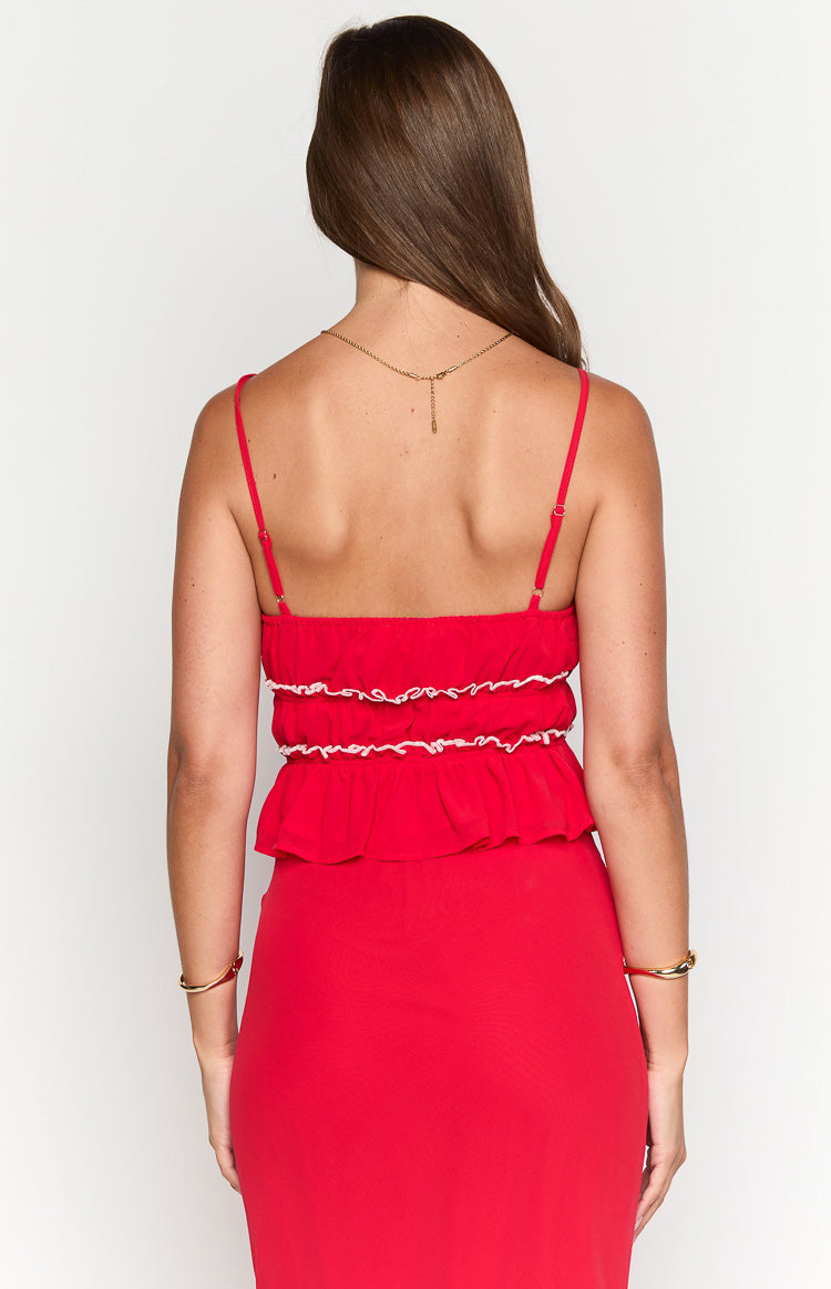Rear view of a red top with thin adjustable spaghetti straps, shirred elastic back with white trim, and a peplum hem