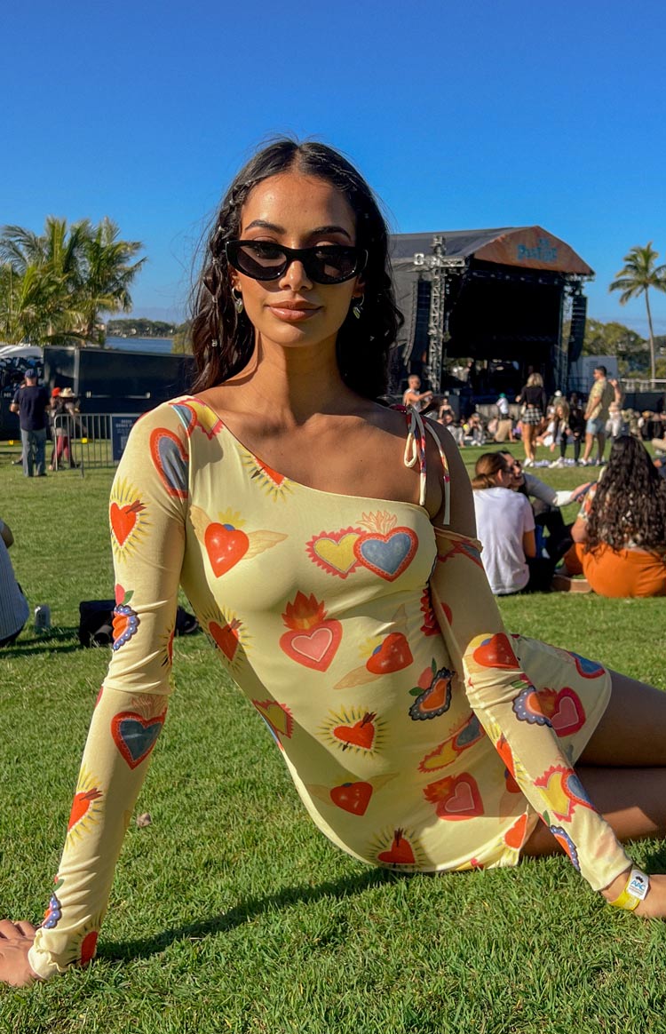 Yellow mesh mini dress with one long sleeve, one-shoulder tie straps, and a vibrant heart print
