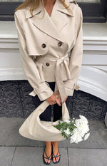 Cream cropped trench coat with double-breasted front, notched lapels, storm flap, shoulder epaulettes, and tied waist belt