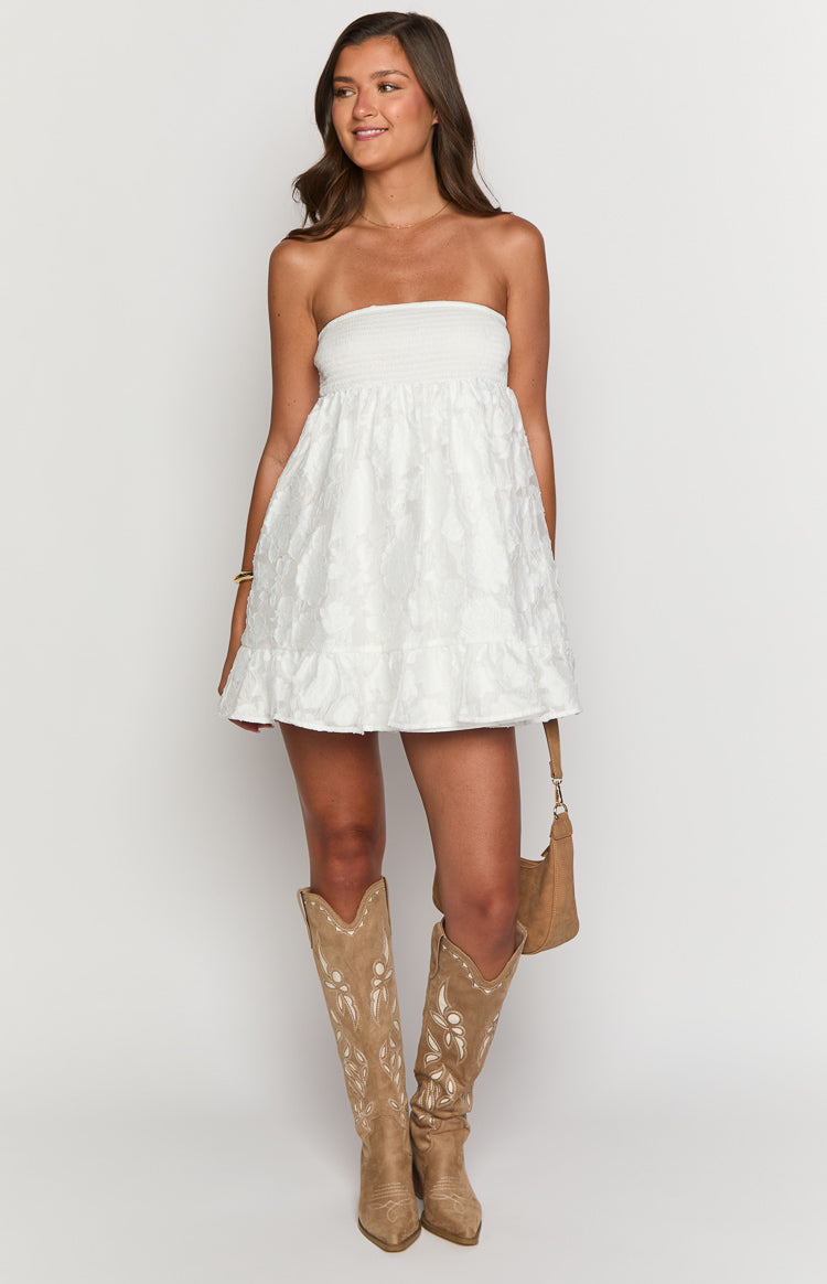 White strapless mini dress with a shirred bust, textured floral pattern on the skirt, and a ruffle hem