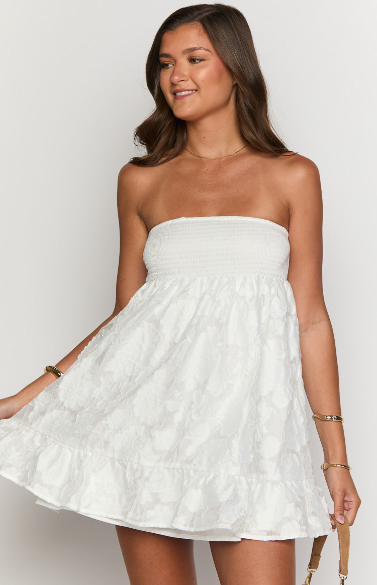 Close-up of the white strapless mini dress showing the shirred bodice and textured floral fabric with a ruffled hem