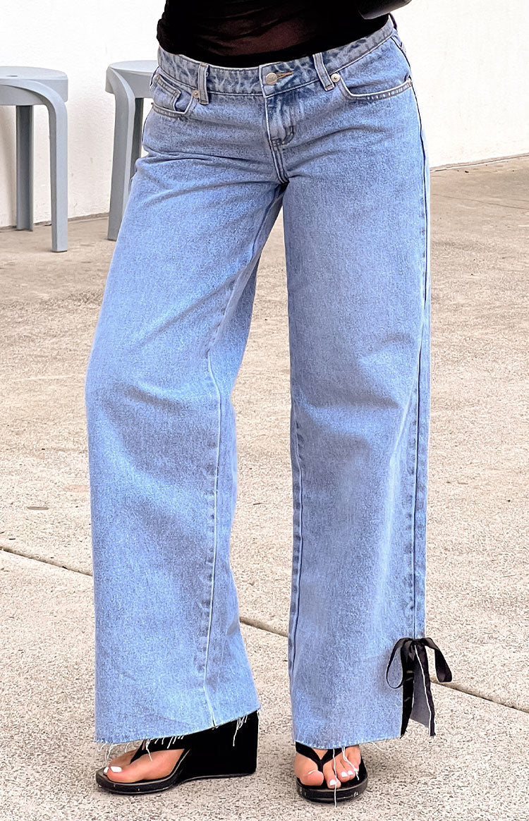 Close-up of light wash denim jeans showing the black bow tie detail at the hem and frayed edges
