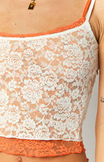 Close-up of the white floral lace fabric of the tank top with orange contrast trim at the neckline and hem