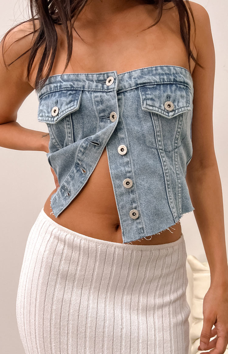 Front view of a light wash denim strapless top with silver buttons and a raw frayed hem