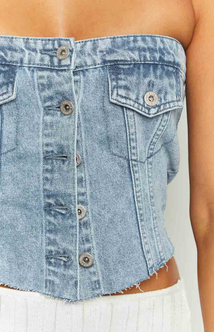 Close-up front view of the light wash denim button top, showing the silver button-front closure, chest flap pockets, and raw frayed hem