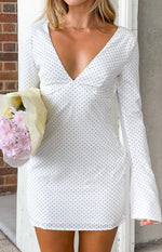 Close-up of the deep V-neckline, fitted bodice, and flared long sleeves of a white polka dot mini dress